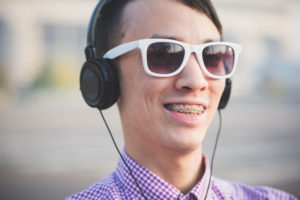 A smiling man wearing braces, headphones and white sunglasses.