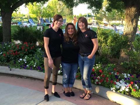 Three women standing in front of a garden with flowers. 